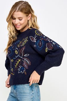 a woman is wearing a blue sweater with colorful flowers on it and has her hands in her pockets