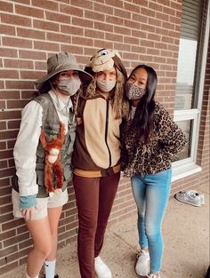 three people wearing masks standing in front of a brick building with one person holding a stuffed animal