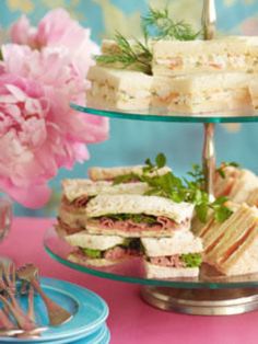 three tiered trays with sandwiches on them and pink peonies in the background