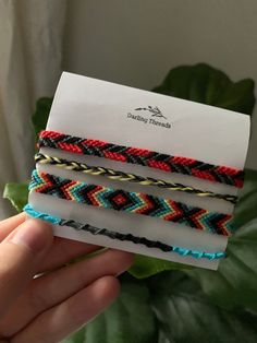 a hand holding four different colored bracelets on top of a white piece of paper