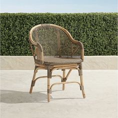 a wicker chair sitting on top of a cement floor next to a hedge covered wall