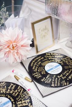 a table topped with black and gold plates covered in writing next to a pink flower