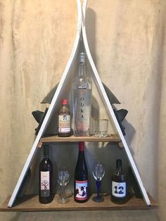 a triangle shaped shelf with bottles and glasses on it, in front of a wall