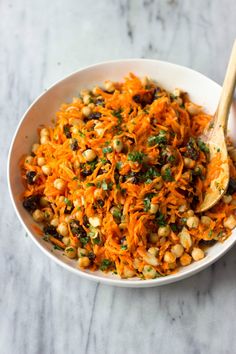 a white bowl filled with carrots and chickpeas next to a wooden spoon