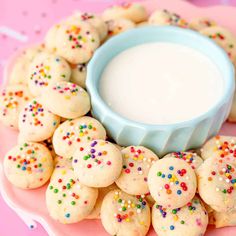 a plate topped with cookies next to a bowl filled with white cream and sprinkles