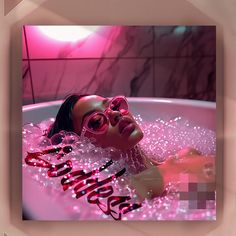 a woman wearing pink sunglasses laying in a bathtub with bubbles and streamers around her