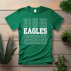 "Show your school spirit in style with our Unisex Eagles Spirit Wear T-Shirt! This eye-catching tee boasts a vibrant repeating pattern of the word \"Eagles,\" making it the perfect choice for spirited fans, athletes, and alumni. Product Details: Design: A bold and dynamic repeating \"Eagles\" pattern that exudes team pride. Material: Crafted from high-quality, ultra-soft cotton blend fabric for maximum comfort. Fit: Designed for both men and women, this shirt offers a relaxed fit suitable for ga College Spirit Wear, Alumni Reunion, Eagles Shirt, Alumni Events, Sports Tee, School Pride, Spirit Wear, Team Sports, Sports Tees