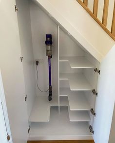 an open closet with shelves and a purple vacuum in the bottom half, under a stair case