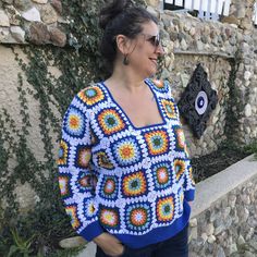 a woman standing next to a stone wall wearing a crocheted sweater and sunglasses