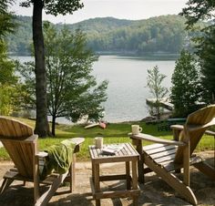 two wooden chairs sitting on top of a sandy beach next to a body of water