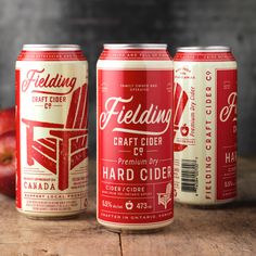 three cans of craft cider beer sitting on a wooden table next to an apple