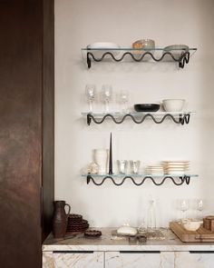 the shelves are filled with dishes and glasses on top of marble countertops in this kitchen