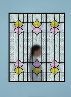 a person standing in front of a stained glass window with gold and white designs on it