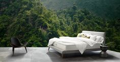 a bed sitting on top of a cement floor next to a lush green forest covered hillside