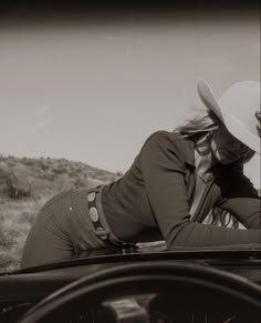 a woman leaning on the hood of a car with a cowboy hat over her head