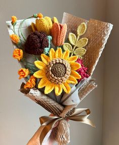 a hand holding a bouquet of flowers made from crocheted yarns and paper