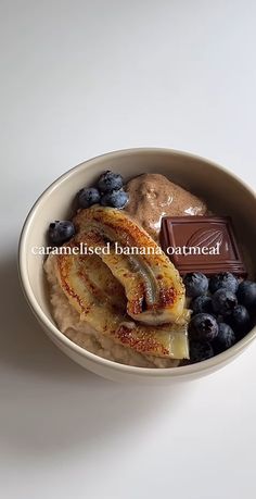 a bowl filled with bananas and blueberries on top of a white table next to a chocolate bar