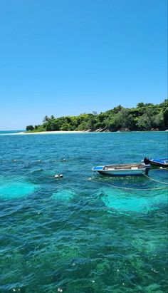 two boats floating on top of a blue ocean next to an island in the distance