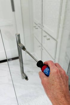 a hand holding a screwdriver in front of a shower door with glass doors