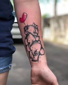 a person with a tattoo on their arm holding a red balloon in the shape of an elephant