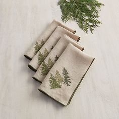 four napkins with pine trees on them are sitting on a table next to some evergreen branches