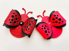 two red and black ladybug hair clips sitting next to each other on a white surface