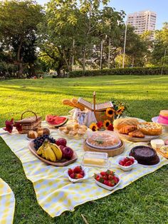 a picnic with fruit, bread and cakes on a blanket in the middle of a park