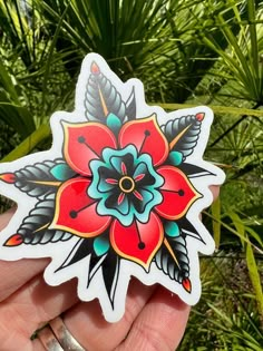 a hand holding a flower sticker in front of some plants