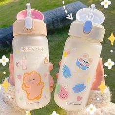 two children's water bottles are held up in front of some flowers and grass