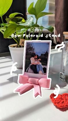 a photo frame with a pink bow on it next to a vase and potted plant