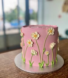 a pink cake decorated with flowers on a wooden table next to a glass window in the background