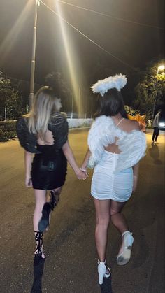 two women dressed in costumes walking down the street at night with their arms around each other