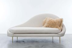 a white couch with a furry pillow on it's back and two gold legs