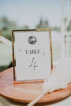 a table sign sitting on top of a wooden table next to a white bird feather