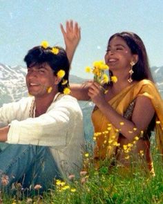 two people sitting in the grass with yellow flowers on their heads and hands raised up