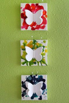 three butterflies are hanging on the wall in front of green paint and white paper with red flowers