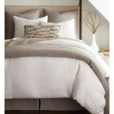 a bed with white linens and pillows in a neutral bedroom setting on a wooden floor