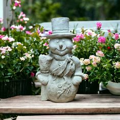 a statue of a teddy bear wearing a top hat and holding a stuffed animal in front of potted flowers