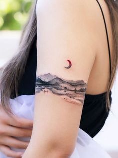 a woman's arm with a tattoo on it that has mountains and a red moon