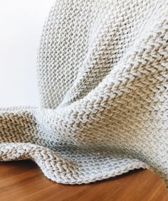 a white knitted blanket sitting on top of a wooden floor