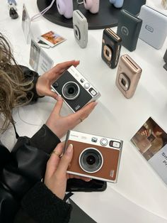 a woman holding an old camera in front of several other cameras on a white table