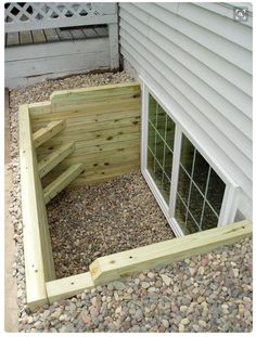 a wooden step leading up to a window in the side of a house with gravel and rocks around it