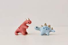 two toy dinosaurs sitting next to each other on top of a white surface with one dinosaur facing the other