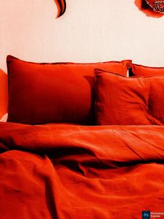 a bed with red sheets and pillows on top of it next to a wall mounted clock