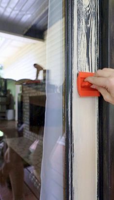 a hand is holding an orange handle on the door to a window that has been painted white