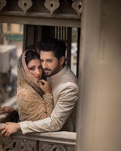 a man and woman standing next to each other in front of a window looking at the camera