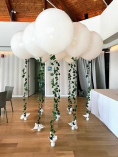 some white balloons and greenery are hanging from the ceiling in an indoor function hall