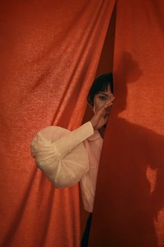 a woman peeking out from behind a red curtain