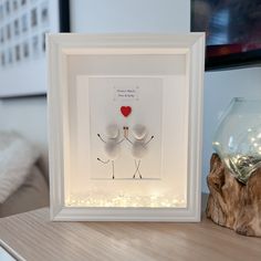 a white frame with two birds in it on a table next to a glass vase