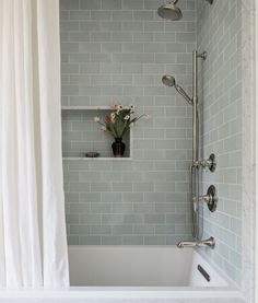 a white bath tub sitting under a window next to a shower head and hand held shower faucet